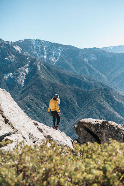 人山上岩石上的年轻女子景观登山者攀岩